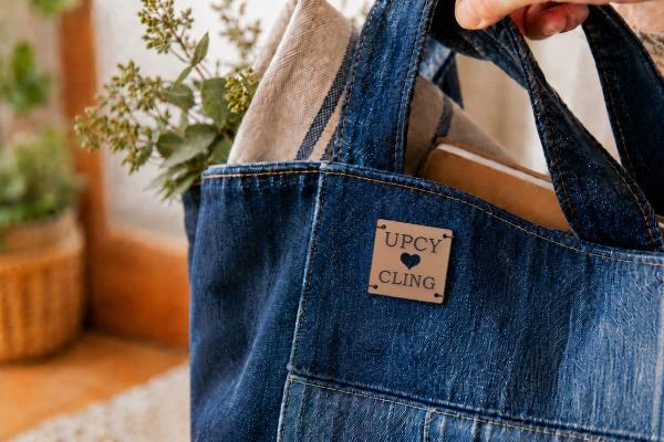 Fyrkantig ljusbrun etikett i kaktusläder med "UPCYCLING" och utstansat hjärta på denimväska.