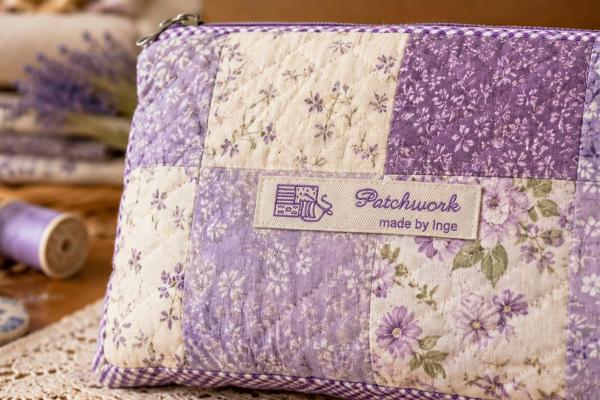 Naturfärgad bomullsetikett med lila text på patchworkväska